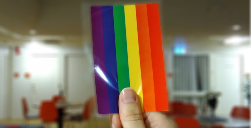 En person håller upp ett kort med en regnbågsflagga